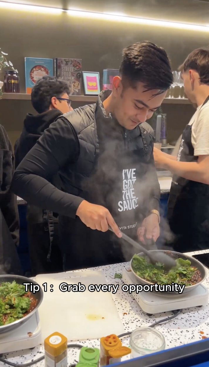 A person wearing an apron cooks vegetables in a pan amidst a steamy atmosphere. Other people are busy in the background. Text at the bottom reads, "Tip 1: Grab every opportunity.